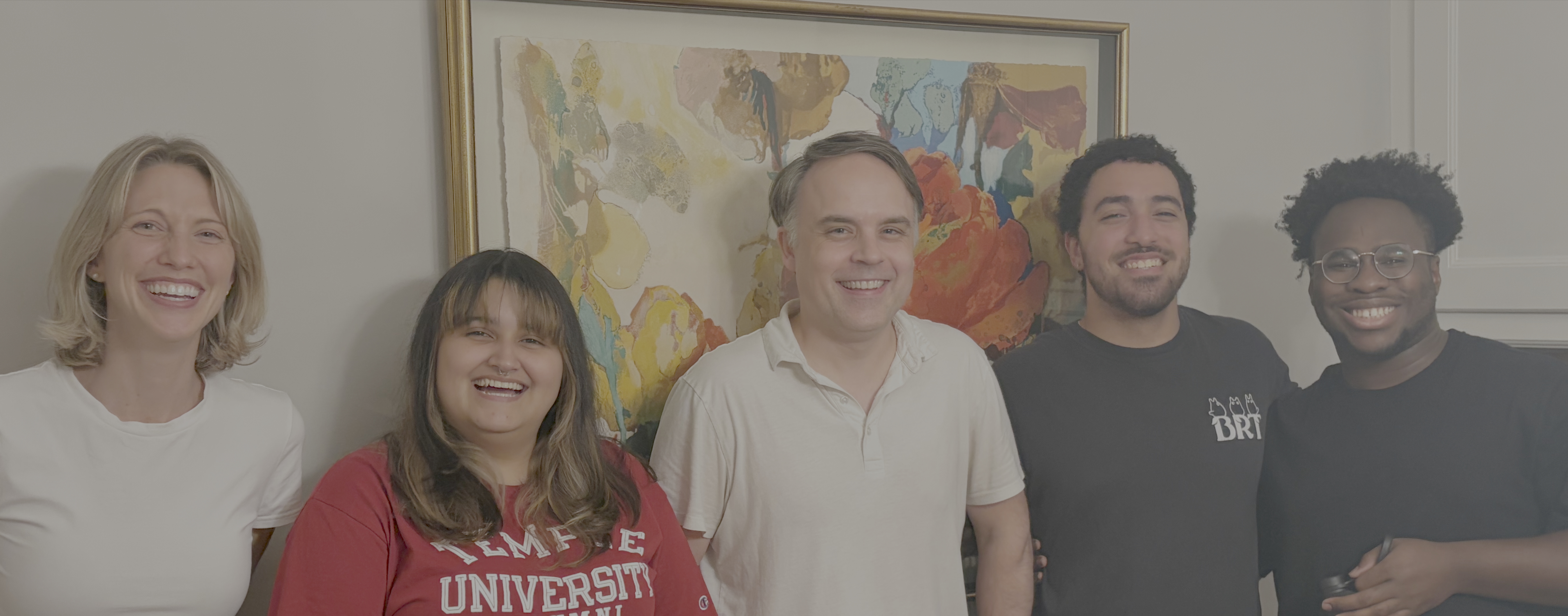 Five members of the Crowther Lab standing together and laughing in front of a framed painting